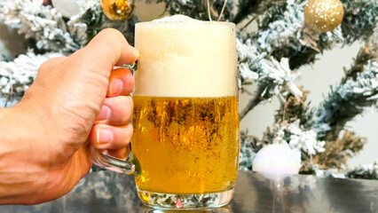 クリスマスツリーを背景に生ビールを持つ男性の手