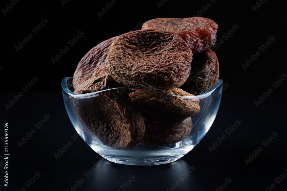 Poster Mountain dried apricots in a glass cup on a black background. Delicious and healthy dried apricots.