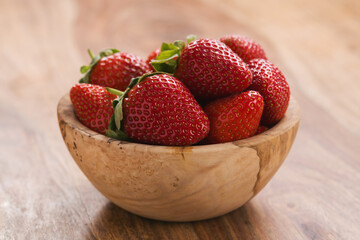 Ripe strawberries in wooden bowl on wood background