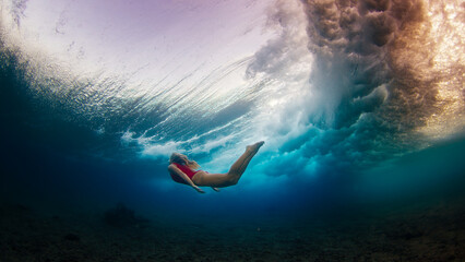 Young slim woman in red suit dives under the breaking wave and swims confidently underwater in the harsh sea environment