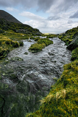 Clear water runs swiftly over rocks. The stream is nestled between grassy, rocky hills.