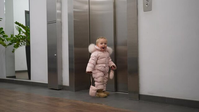 Young child dressed in a pink winter coat walks eagerly toward an elevator in a contemporary indoor setting, showcasing excitement for the ride ahead