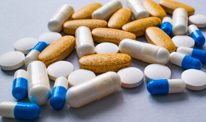 A collection of various pills, capsules, and supplements scattered on a gray surface.