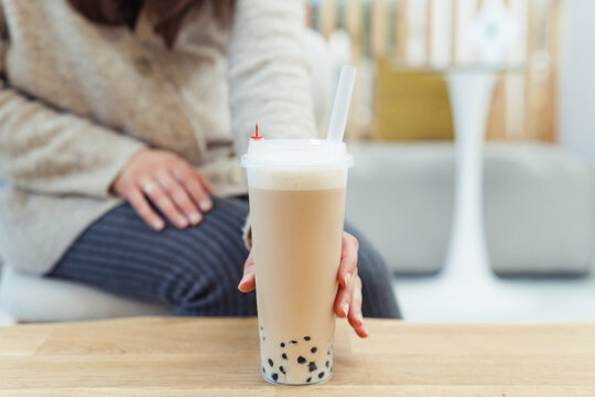 Close-up of a woman in a  coffee shop holding a cappuccino bubble coffee with tapioca pearls