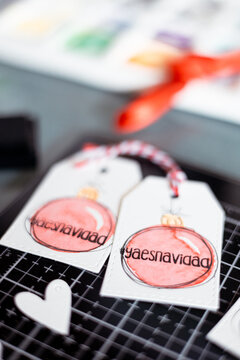 Close-up overhead view of two handmade Christmas gift tags with watercolour painted Christmas baubles and the words ya es navidad