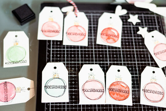 Overhead view of handmade Christmas gift tags with watercolour painted Christmas baubles and the words ya es navidad