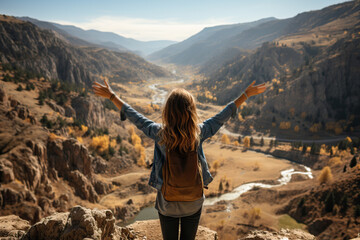Naklejka premium Rear view of a girl sitting with her arms raised and contemplating the beauty of the mountains and river.