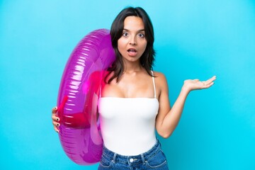 Young hispanic woman holding air mattress donut isolated on blue background with shocked facial expression