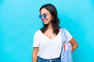Young caucasian woman holding a beach bag isolated on blue background looking to the side and smiling