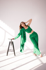 Kobieta w zielonym kombinezonie przy naturalnym świetle padającym z okna oparta o czarnego hokera © robertpstryka