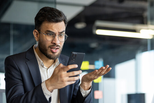 Mature man businessman gestures emotionally holding hone in office . The individual's facial expression and hand movement signify surprising or frustrated reaction, unexpected news or communication