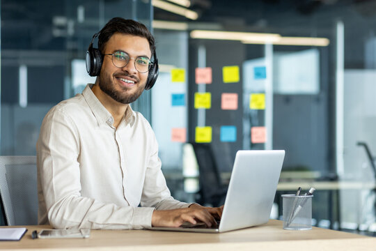 Mature man businessman enjoying work using his laptop and headphones in a contemporary workspace. Smiling and focused, showcasing productivity and engagement in a professional setting