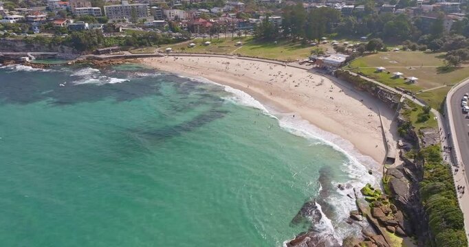 Aerial drone view of Bronte Beach in Sydney, Australia, featuring turquoise ocean water, golden sand, rolling waves, and scenic Pacific coastal landscapes from above.