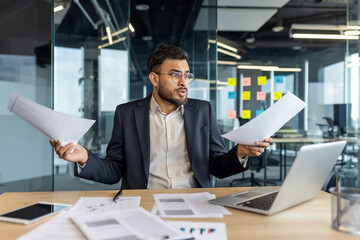 Mature man businessman in a modern office examining paperwork, appearing stressed. The image depicts a professional environment emphasizing multitasking, decision-making, and workload management.