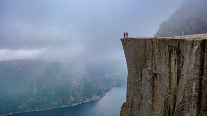 Preikestolen, Norway, A hiker stands on the edge of a cliff with arms outstretched, taking in the breathtaking view of the Norwegian fjords shrouded in mist