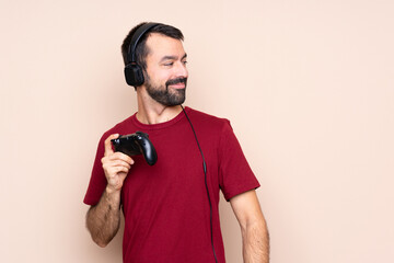 Man playing with a video game controller over isolated wall with arms crossed and happy