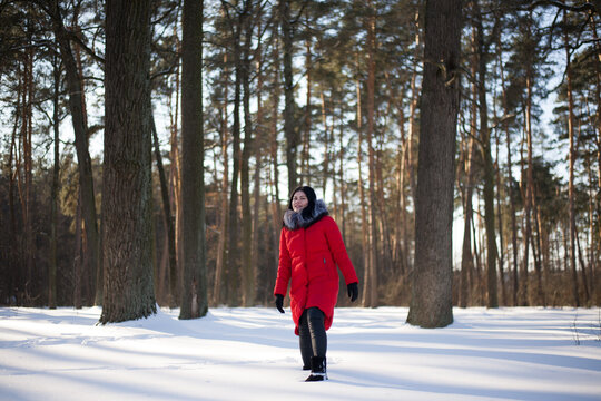 photo with a young woman in the winter forest. girl in a snowy park. in a red jacket on the banks of a frozen river. winter walk in nature. Cold season. Beautiful girl, sunny day. - Powered by Adobe