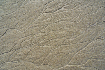Sand with natural patterns and textures created by water movements. These wave-like lines showcase the beauty of nature.