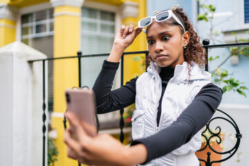 Young latin american woman taking a selfie, raising sunglasses with surprised expression