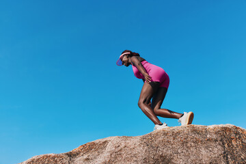 Woman in pink sportswear running on a rocky terrain under a clear blue sky