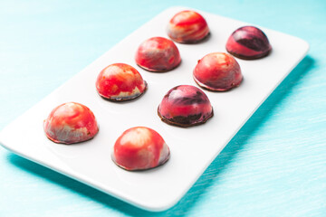 Assorted multi-colored homemade chocolates. Modern hand-painted chocolates on a white plate on a blue background. Product concept for chocolatier. Selected focus