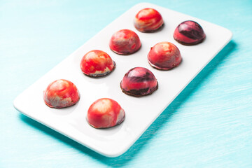Assorted multi-colored homemade chocolates. Modern hand-painted chocolates on a white plate on a blue background. copyspace.Product concept for chocolatier. Selected focus.