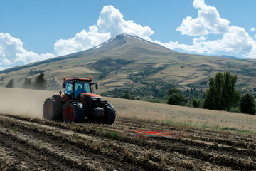 Obraz premium Tractor plowing field, mountain background.