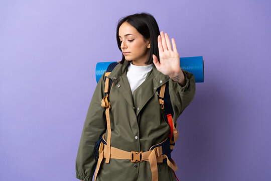 Young mountaineer woman with a big backpack over isolated background making stop gesture and disappointed