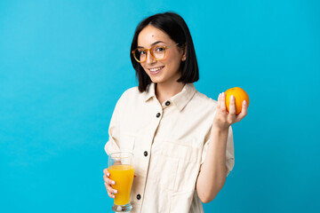 Young caucasian woman isolated on blue background holding an orange and an orange juice