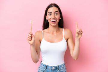 Young caucasian woman brushing teeth isolated on pink background pointing up a great idea