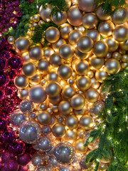 A vibrant display of shimmering gold and purple ornaments fills the space, illuminated by soft lights. The arrangement creates a festive atmosphere, enhancing the holiday spirit.