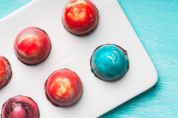 Assorted multi-colored homemade chocolates. Modern hand-painted chocolates on a white plate on a blue background. copyspace.Product concept for chocolatier. Selected focus.