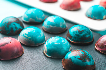 Assorted multi-colored homemade chocolates. Modern hand painted chocolates on white and black plates on a blue background. Product concept for chocolatier. Selected focus copyspace