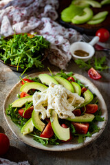 Salad with avocado, tomatoes, arugula and cream cheese on a white plate on a gray background. Vertical photo