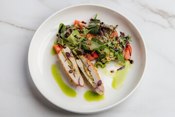 Slices of grilled chicken breast stuffed with pesto, paired with a fresh salad of tomatoes and arugula, elegantly arranged on a white plate. Restaurant or cafe menu, cookbook recipe