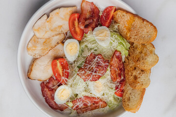 Fresh caesar salad featuring grilled chicken, crispy bacon, halved boiled eggs, crunchy croutons, parmesan cheese, and ripe cherry tomatoes in a white bowl. Restaurant or cafe menu, cookbook recipe