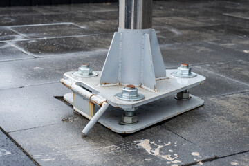 A metal pole base firmly attached to a wet tiled floor, showcasing bolts, a latch, and a clean...
