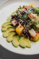 Colorful salad with grilled chicken, creamy avocado, sweet mango, crispy croutons, and parmesan, topped with dressing and presented on a white plate. Restaurant or cafe menu, cookbook recipe