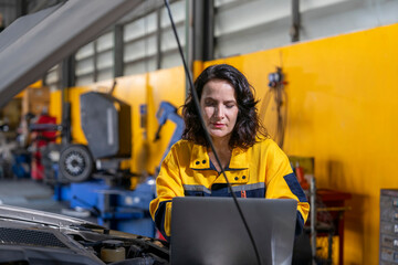 woman middle aged experienced mechanic in uniform using laptop examining car engine,concept of garage service,business,industry
