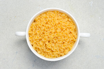 White ceramic bowl of raw pasta. Top view. On a light stone background.