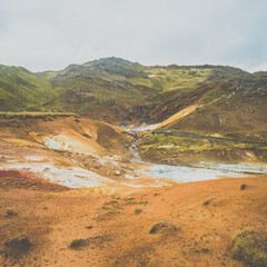 Geothermal landscape at Seltún, Reykjanes Peninsula, Iceland, showcasing vivid sulfuric deposits, steaming vents, and rugged volcanic terrain under an overcast sky.