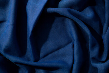 Navy or dark blue fabric wavy spiral crumpled background texture with copy space in the center.