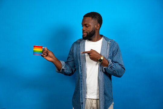 Young man pointing at a rainbow mug against blue background