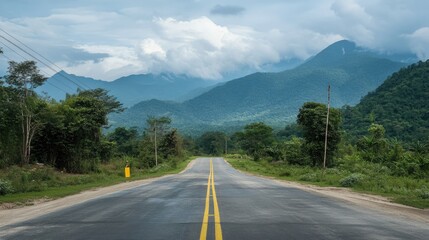Naklejka premium Serene Vista of an Empty Road with Yellow Markings, Framed by Majestic Mountains and Gentle Clouds