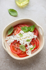 Serving tray with red tomatoes, stracciatella di bufala and green basil, vertical shot on a beige stone background, high angle view