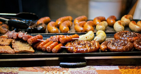 Grilled sausages of various types on a sizzling grill, showcasing a mix of coiled, traditional, and herb-infused varieties. Perfect for concepts like street food, BBQ, culinary traditions, or outdoor 