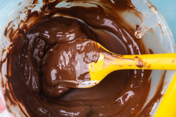 Tempering dark professional chocolate. The process of making handmade chocolates. Bowl with melted chocolate and yellow spatula on blue background