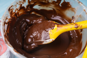 Tempering dark professional chocolate. The process of making handmade chocolates. Bowl with melted chocolate and yellow spatula on blue background