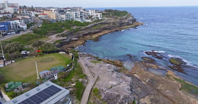 Aerial drone view of Tamarama Point in Sydney, Australia, showing rugged coastal cliffs, turquoise ocean water, rolling waves, and scenic Pacific coastline from above.