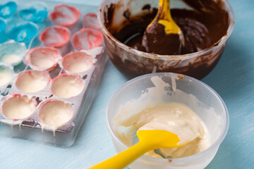 The process of making handmade chocolates. A candy mold with colorful dyes and bowls with white and dark chocolate.